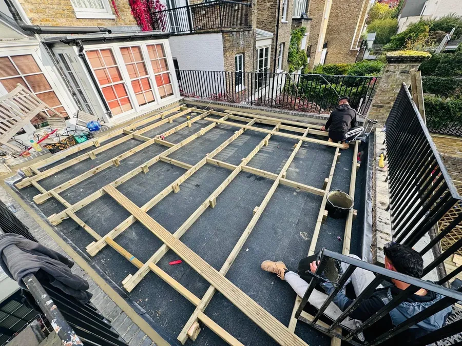 Team framing a new flat roof deck behind iron railings, Imperial Roofcraft roofing job in London